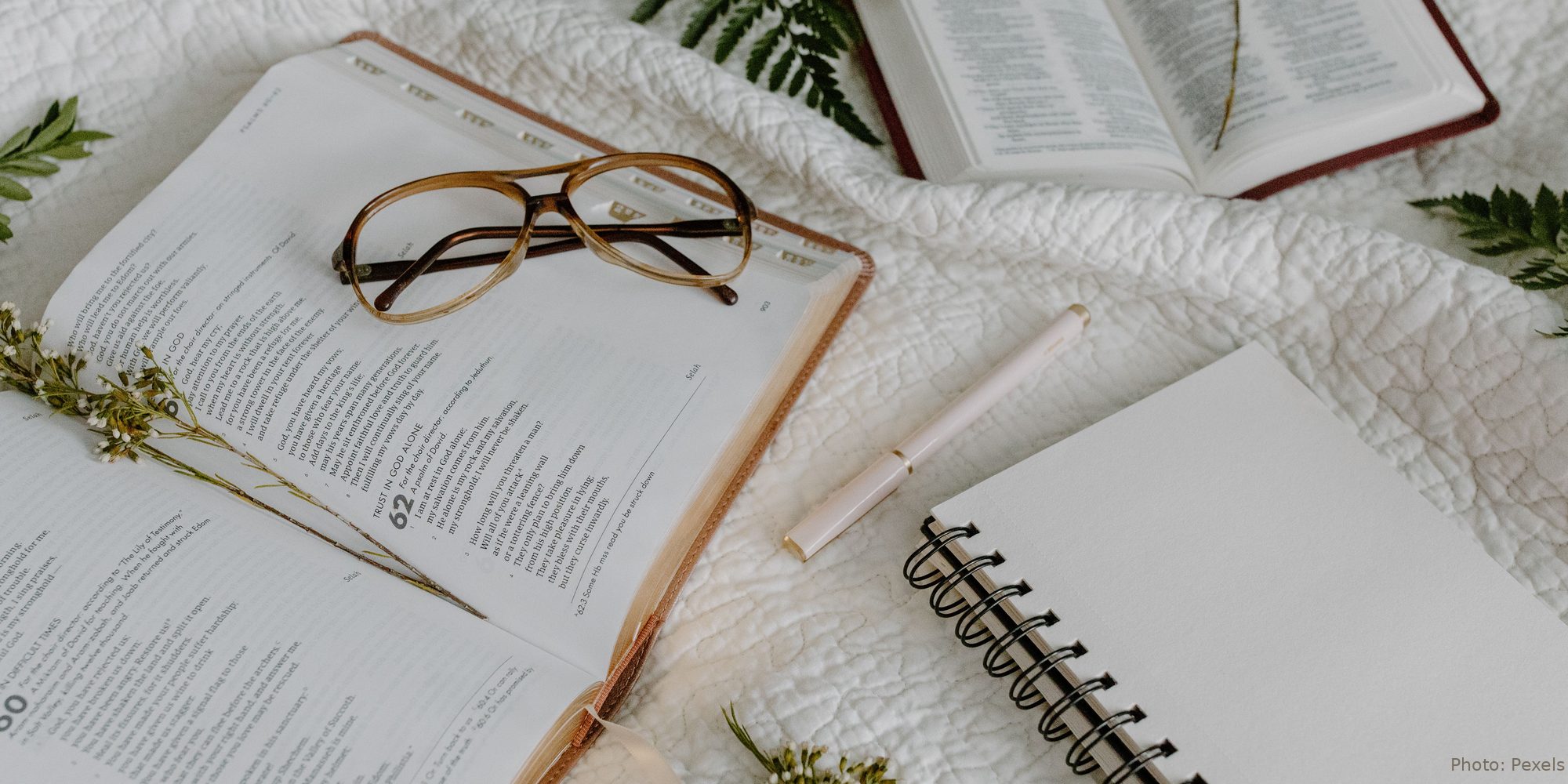 An open Bible rests on a white quilt at Psalm 62 — Trust in God Alone — beside reading glasses and a journal.