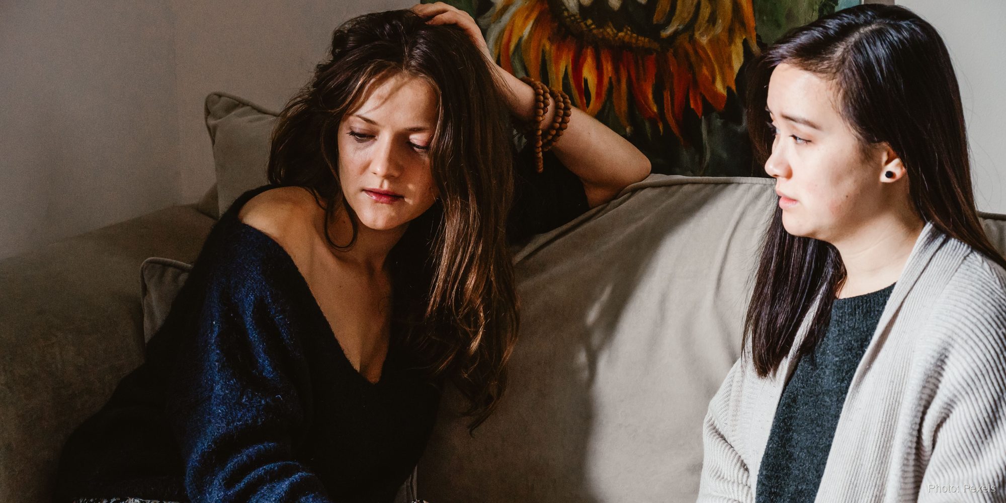 Two women talk closely on a couch, one listening with quiet attention while the other works through a hard decision.