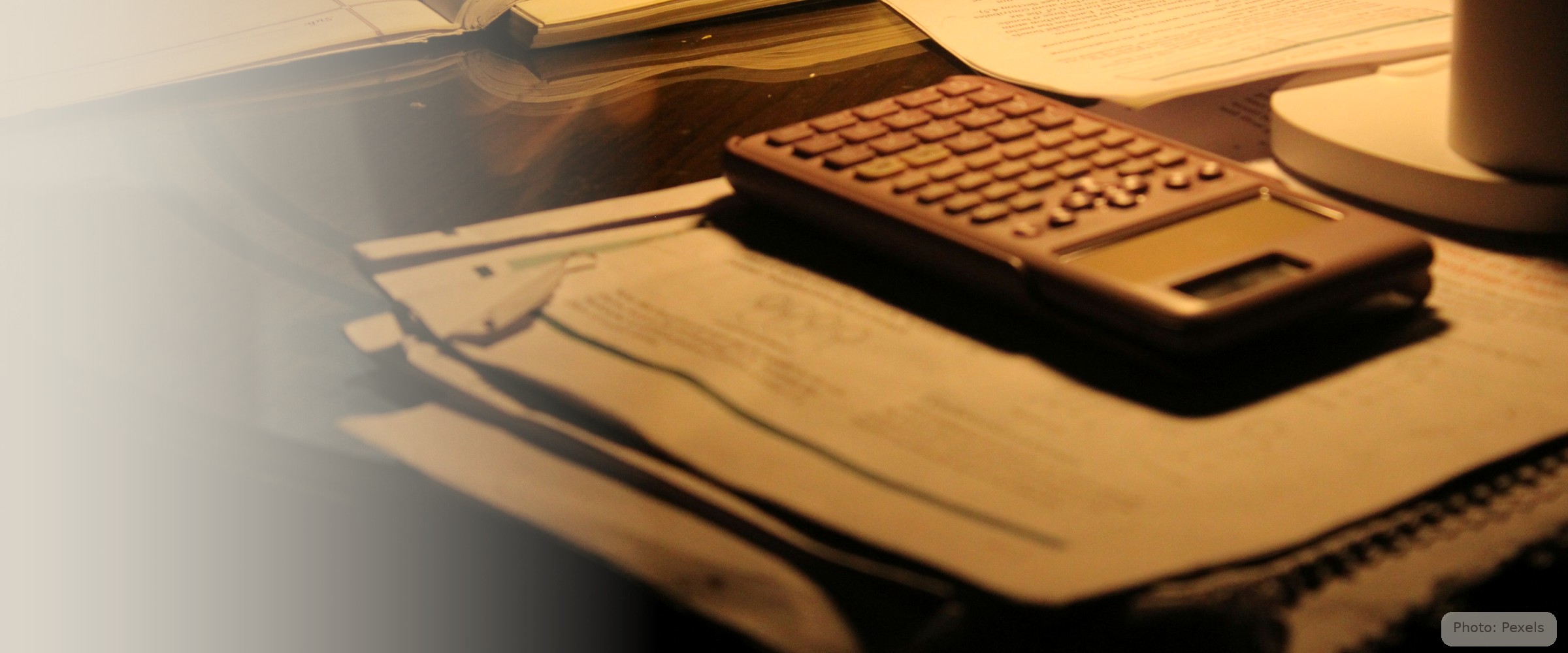 A calculator and papers sit under a single lamp on a table at night — the quiet math of a rent that no longer fits.
