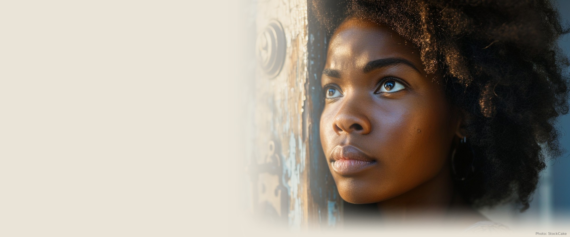 A woman stands quietly at a heavy studded door in warm evening light, looking up.