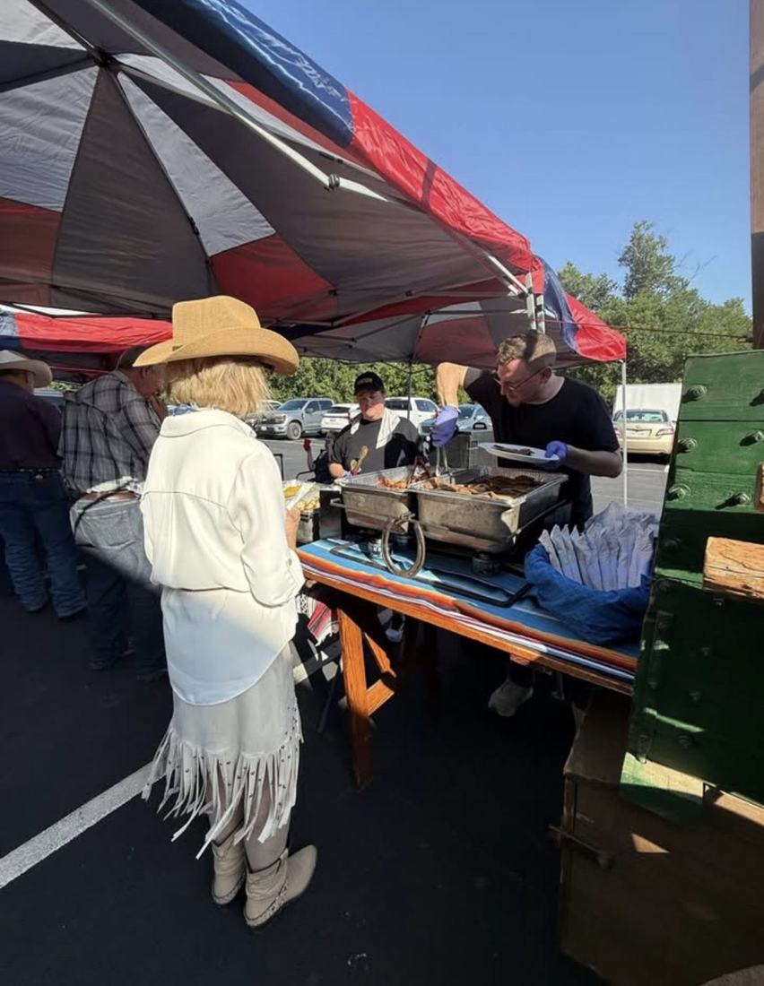A guest is served barbecue from chafing dishes under a tent in the car park.