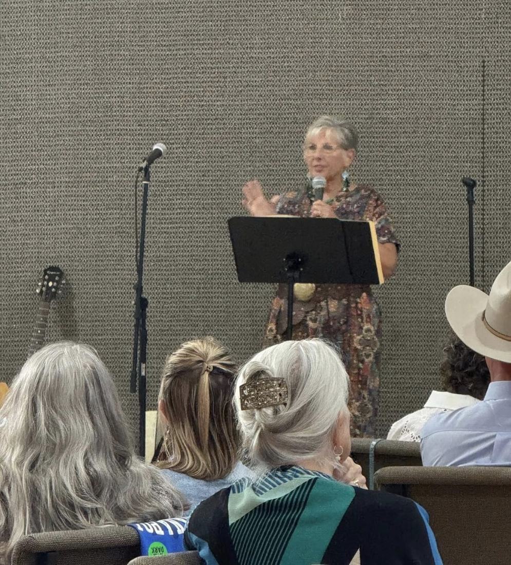 A speaker addressing the seated room from a lectern with a microphone.