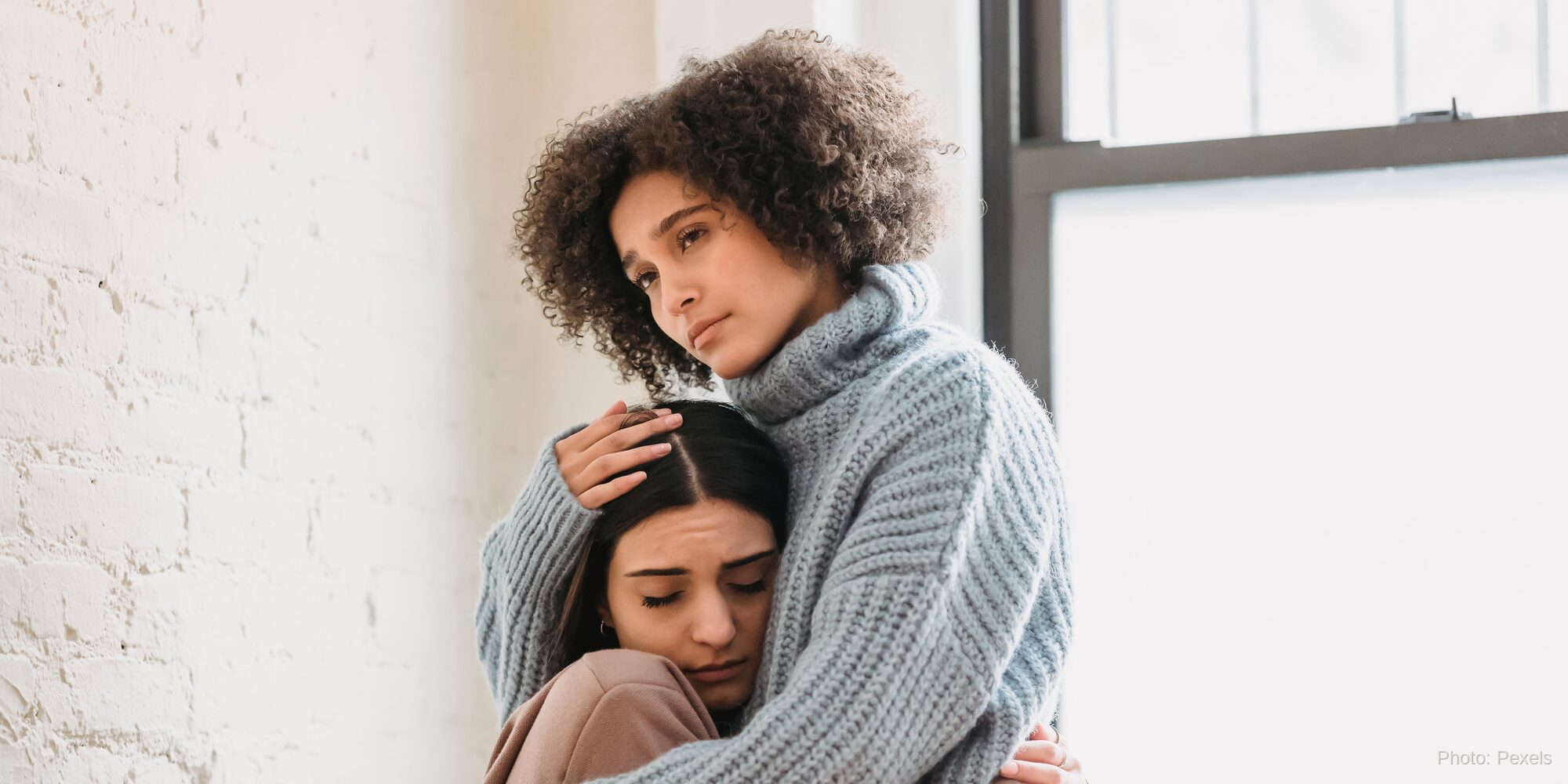 A woman rests her head on a friend's shoulder, met with a steady hand and no judgment — the opposite of hiding in shame.