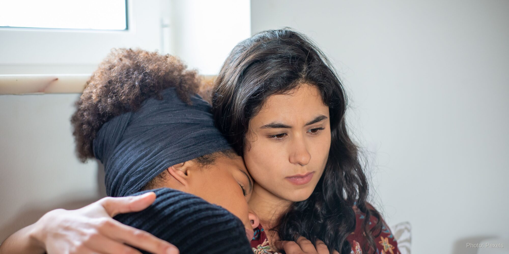 A woman rests safely in a friend's arms, met with quiet, steady attention — presence that says, I'm not going anywhere.