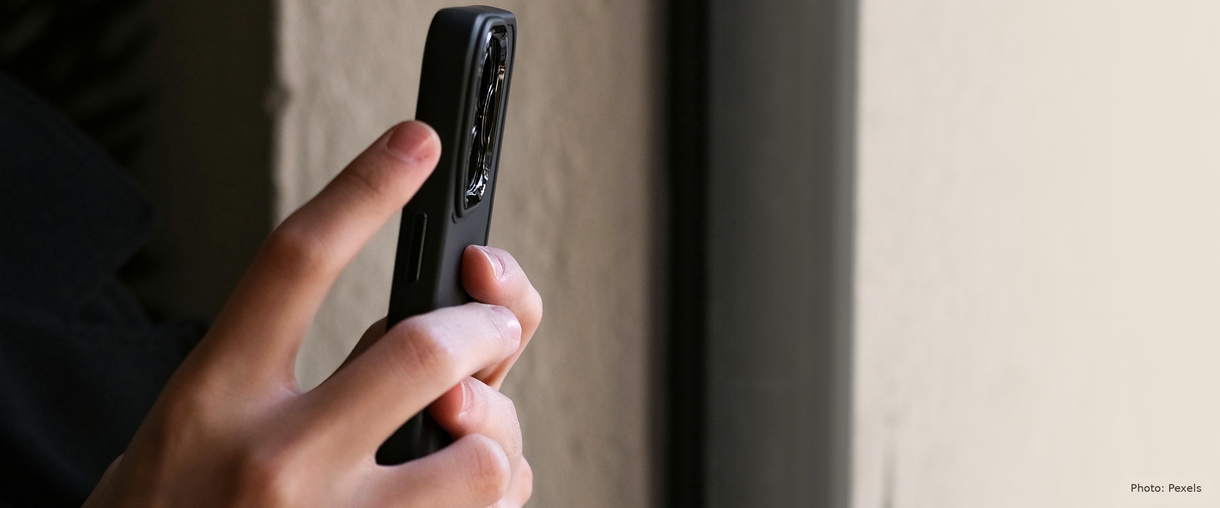 A hand holds a phone in a quiet doorway — restrained, symbolic, no face, no narrative.
