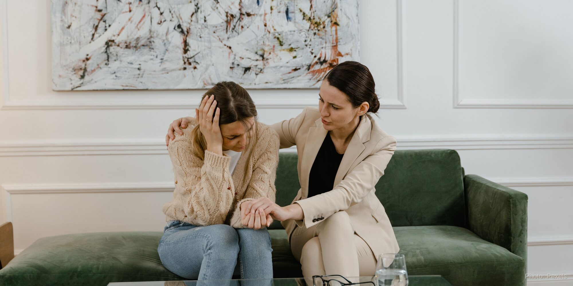 A counselor sits close, hand gently on her shoulder, meeting a woman's distress with steady presence rather than control.